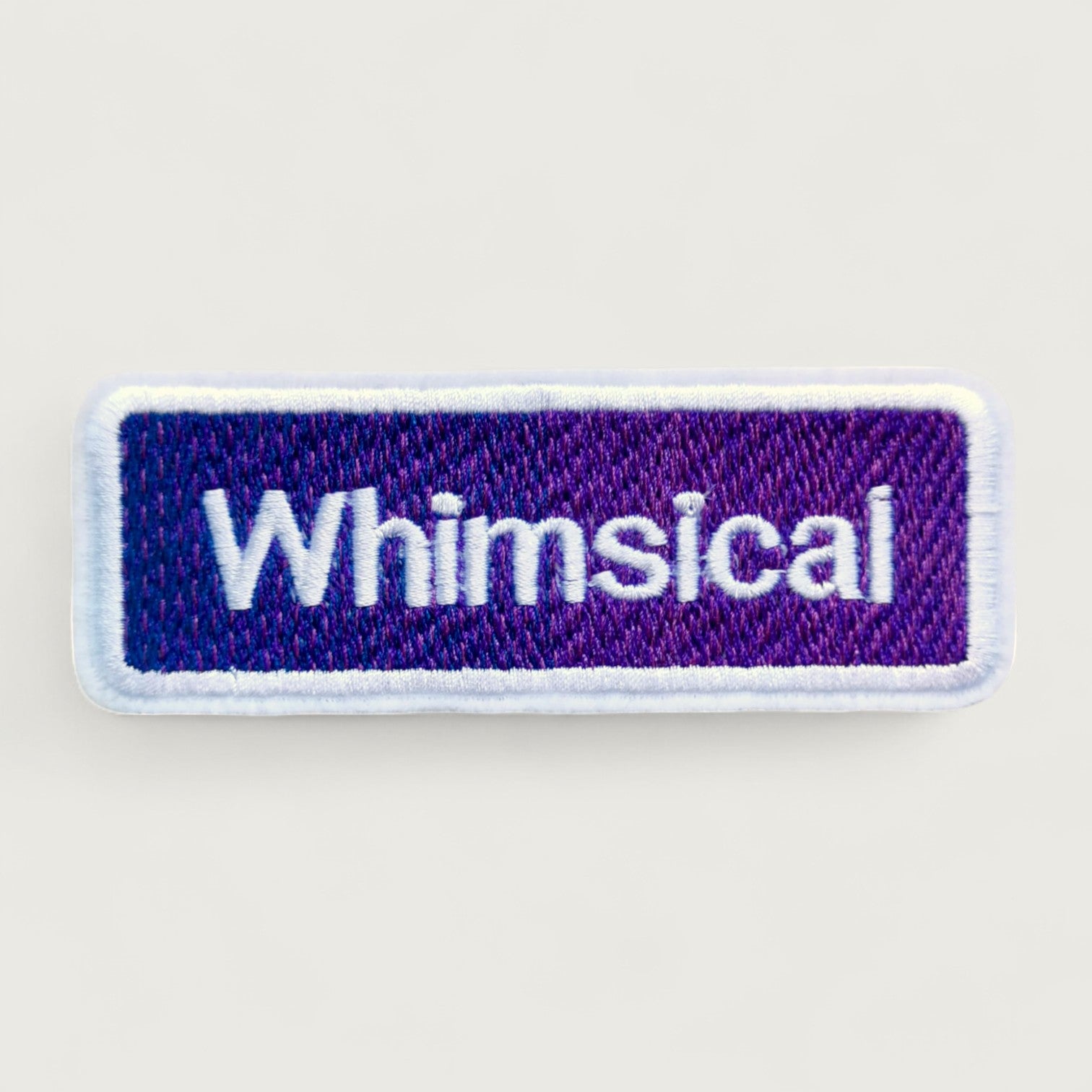 Rectangular purple embroidered patch with white text 'Whimsical' and a soft white border – fun aesthetic patch for playful fashion or accessories