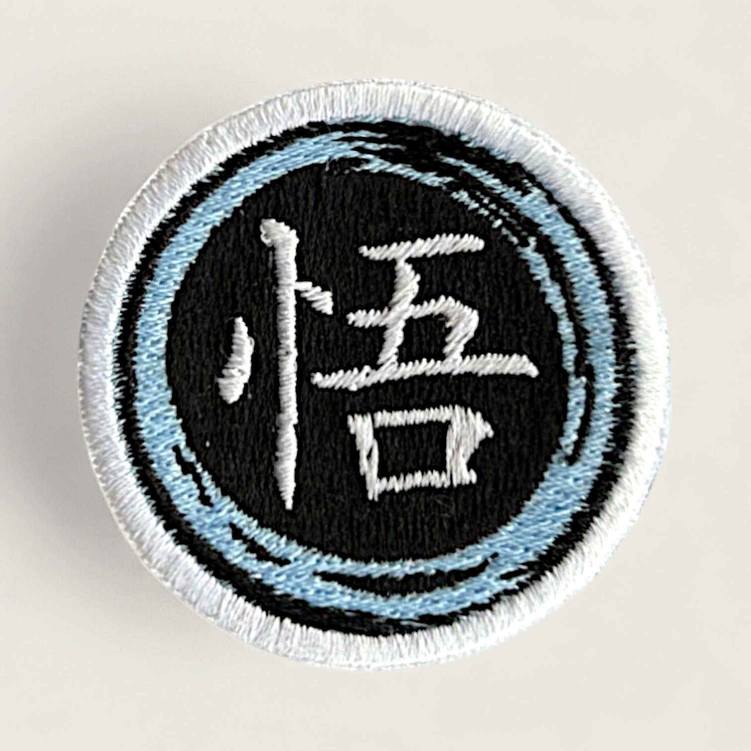 Round embroidered patch featuring the white Japanese kanji "悟" (Go, meaning "enlightenment" or "awareness") on a black background, surrounded by a stylized light blue and white swirl border. Inspired by anime and martial arts aesthetics, ideal for jackets, backpacks, or cosplay.
