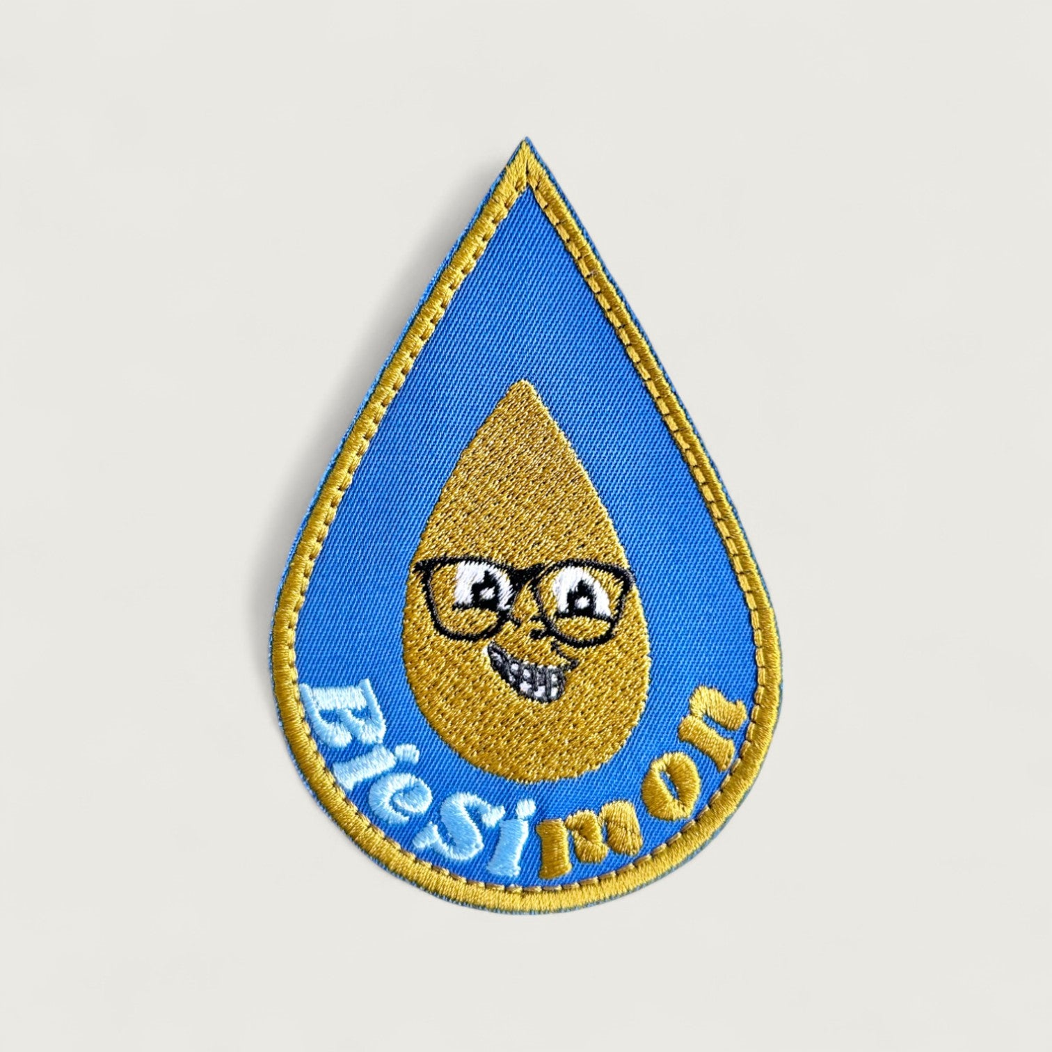 Teardrop-shaped embroidered patch with a smiling golden oil drop character wearing glasses and the text 'BioSimon' – fun eco-themed patch for biofuel or sustainability brands