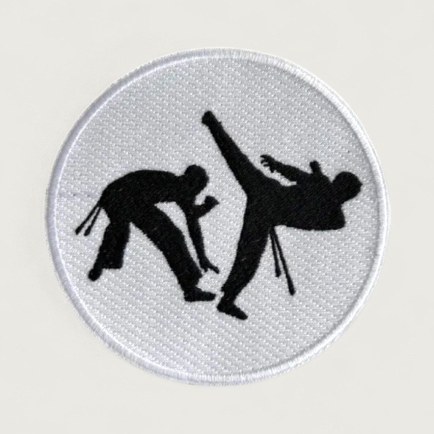Round embroidered martial arts patch featuring two black silhouette figures practicing high kicks on a white background, ideal for taekwondo or karate uniforms.