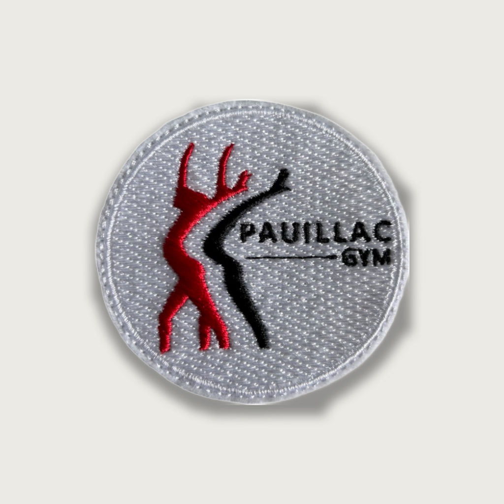 Round embroidered patch with red and black silhouettes of gymnasts and “PAUILLAC GYM” text on white background