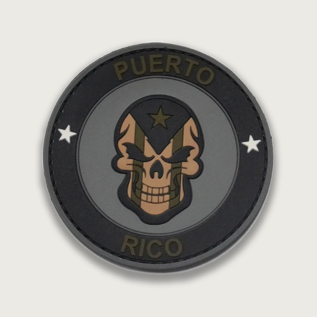 Military-style PVC patch featuring a tactical skull design with Puerto Rico flag elements and subdued army colors. Durable rubber patch ideal for tactical gear, backpacks, or jackets.