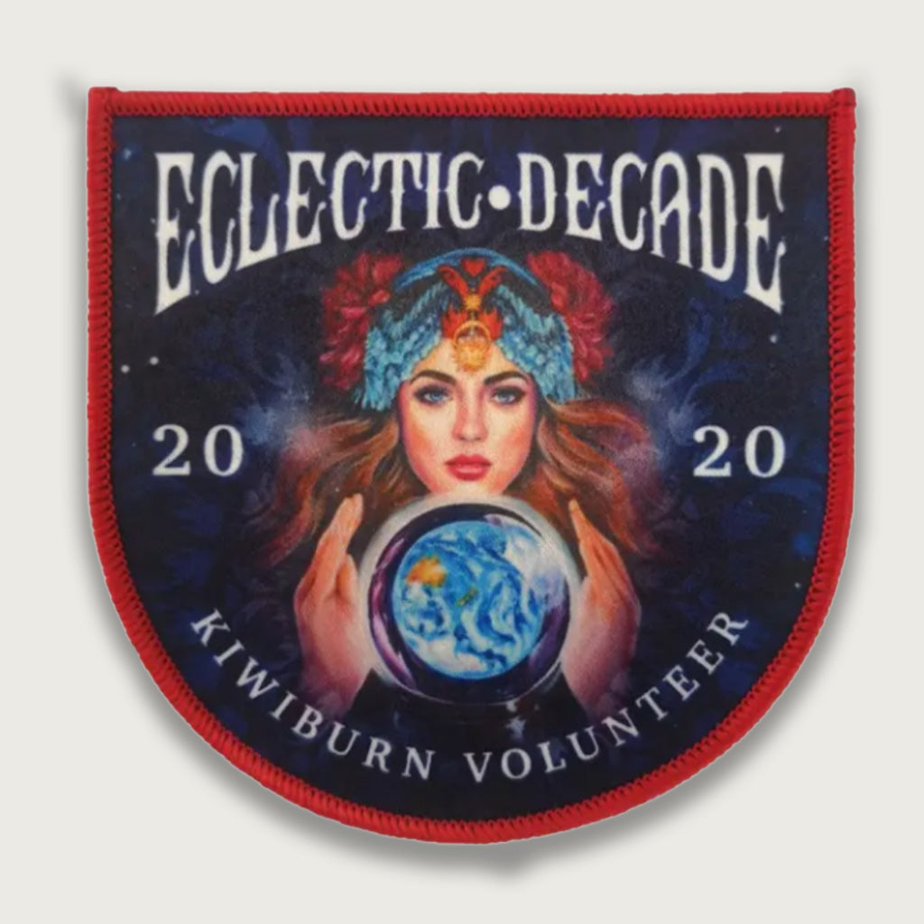 Sublimated 2020 Kiwiburn volunteer patch featuring a mystical woman with a crystal ball and feathered headpiece, with the text "Eclectic Decade" above. Psychedelic festival badge with vivid, artistic design